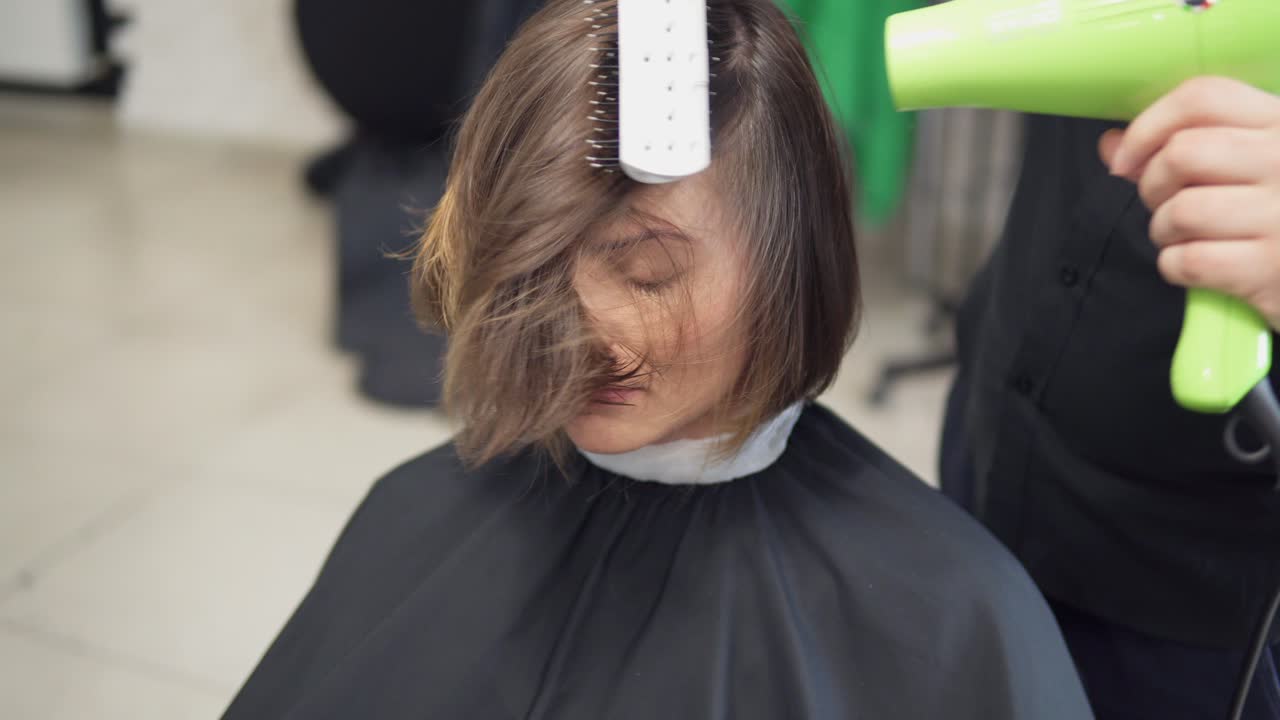 젊은 여성이 헤어 살롱에서 머리카락을  ⁇ 고 있습니다. 남성 헤어 드라이어는 헤어 드라이어를 사용하여 머리카락을 건조하고 있습니다. 4k로 촬영