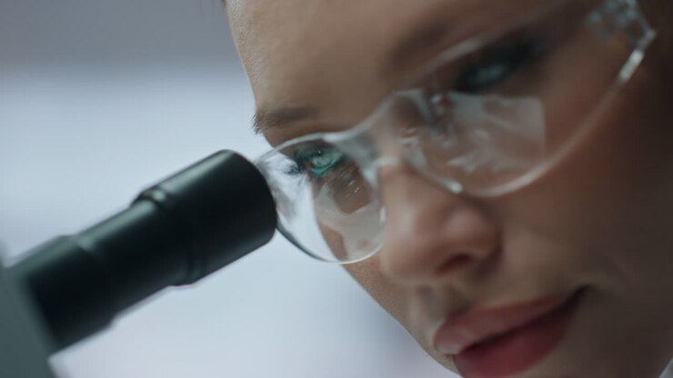 Primo piano di uno specialista in microbiologia che osserva al microscopio esplorando micro campioni.