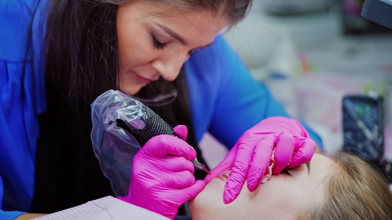 Lips pigmentation process. Professional tattooist doing permanent make-up on woman's lips in a beauty salon. Cosmetology concept.