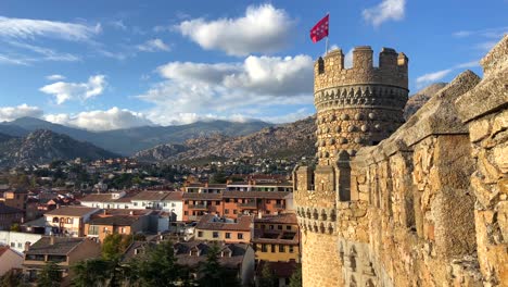 Static-scenic-slow-motion-clip-of-Madrid-flag-waving-with-the-wind-on-the-top-of-a-battlement-of-a-medieval-castle-with-Manzanares-el-Real-village-views
