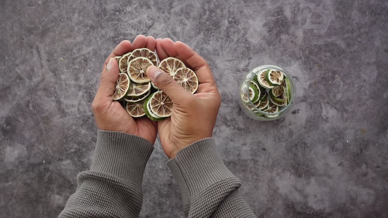 Hands Holding Dried Lime Slices Against a Dark Background