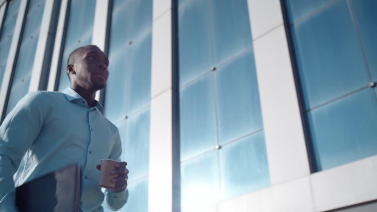Businessman walking outside in front of a modern building with a coffee cup