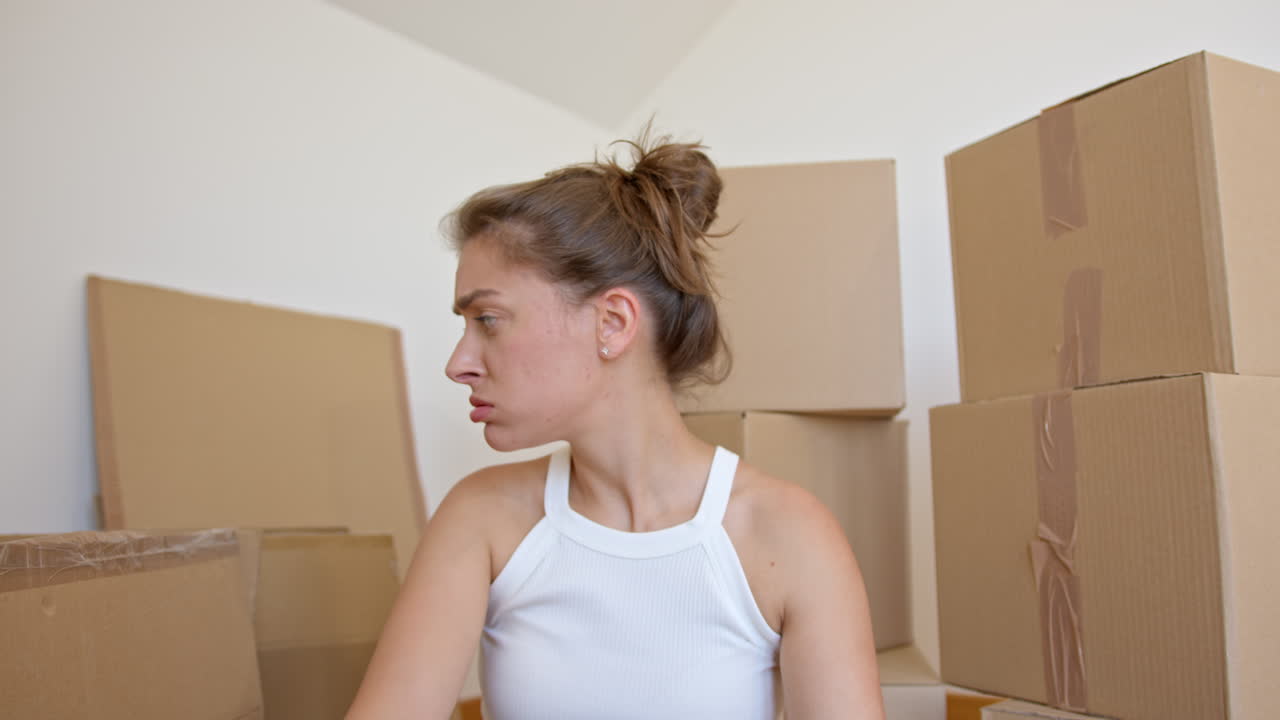 Worried woman looking around unsure where to start unpacking moving boxes. Close up