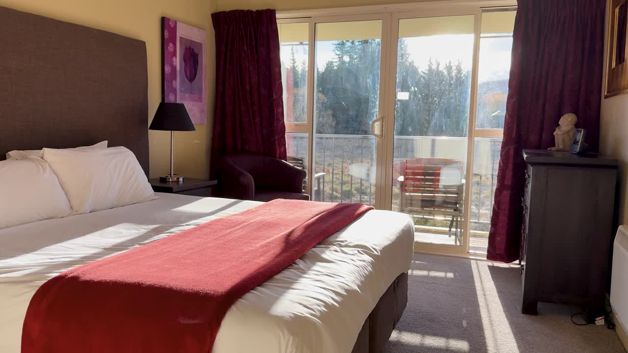 Camera moves through an open door into a bright, modern bedroom with large windows, red accents, and natural sunlight streaming in from outside