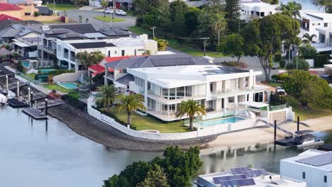 aerial footage smoothly pans over a modern waterfront mansion with pool, private dock, and lush landscaping in a sunny gold coast neighborhood