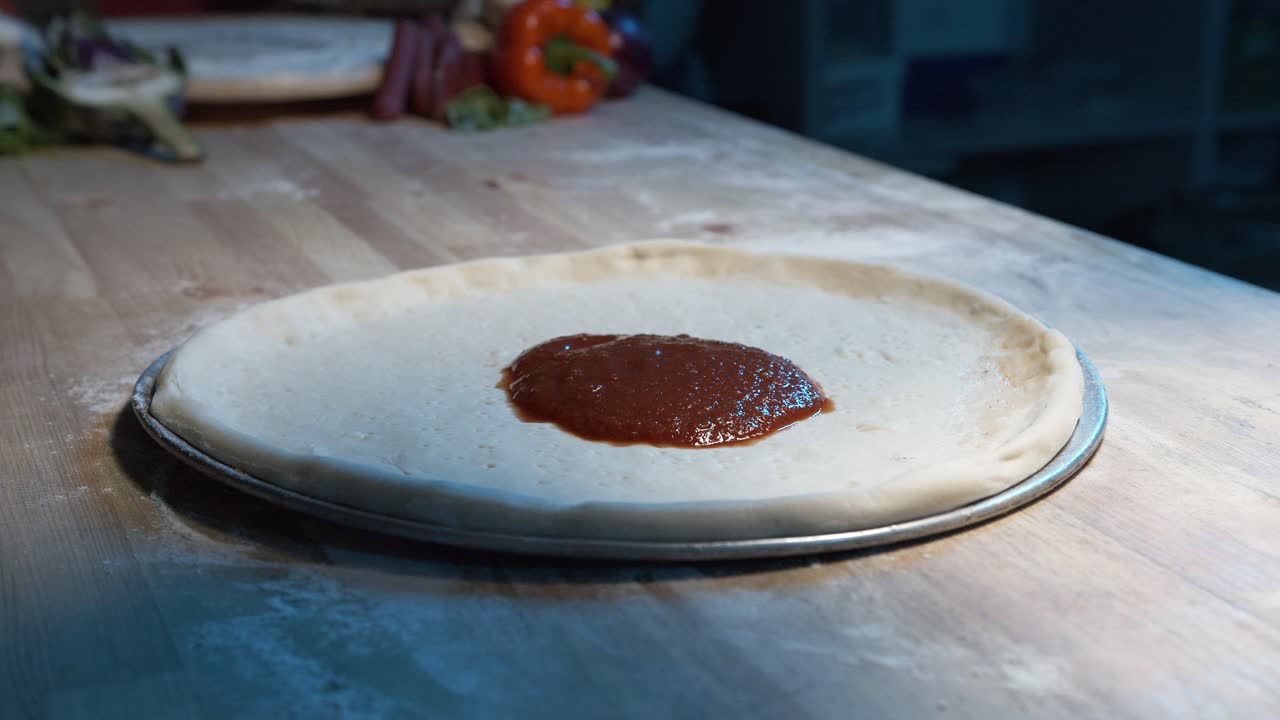 masa de pizza en una bandeja de acero sobre un mostrador de madera mientras un chef experimentado le pone salsa roja con un ácido