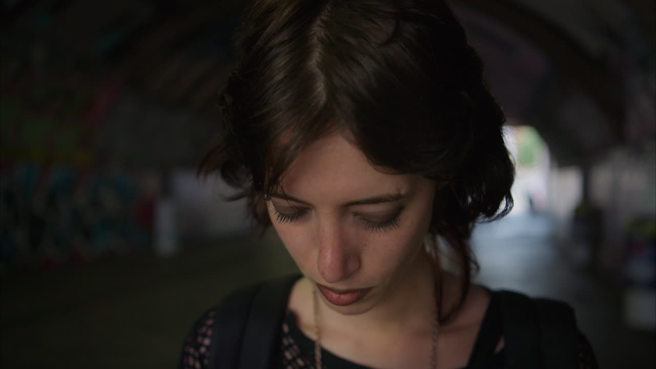 불안한 젊은 대안 스타일의 여성은 런던 시티 스트리트에서 그래피티로 인 벽이있는 어두운 지하 통로를 따라 실시간으로 걸어가고 있습니다.