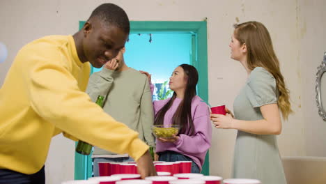 happy multiethnic young friends playing beer pong at home