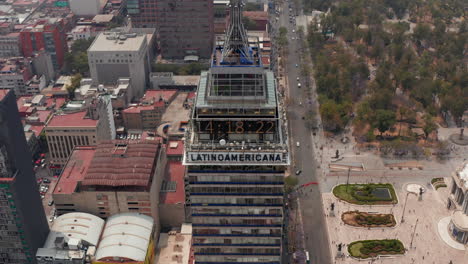 Drone-camera-flying-backwards-and-tilting-up.-Close-up-view-of-number-clock-on-top-of-tall-building-changing-to-panoramic-view-of-Mexico-city-downtown-with-strongly-polluted-air.