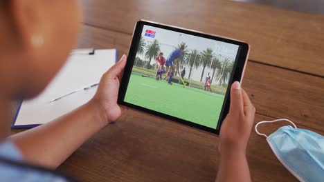 composite of woman sitting at table with face mask, watching hockey match on tablet