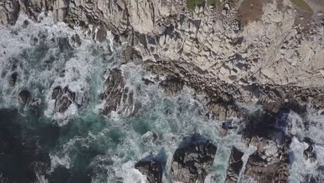 foamy sea waves crashing on rocky cliff along the coast in california - aerial orbit