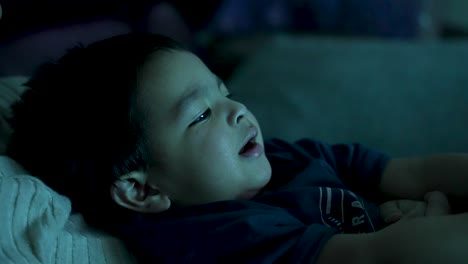 británico asiático de 18 meses se relaja en el sofá, absorto en ver la televisión, con suaves reflejos de luz proyectando una atmósfera acogedora, encarnando la esencia del tiempo libre de casa tranquila