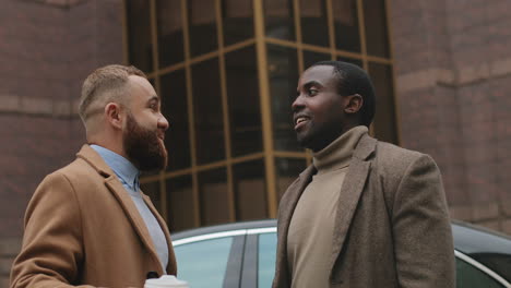 close-up van blanke en afro-amerikaanse zakenman die lacht terwijl ze in de herfst een leuk gesprek hebben op straat