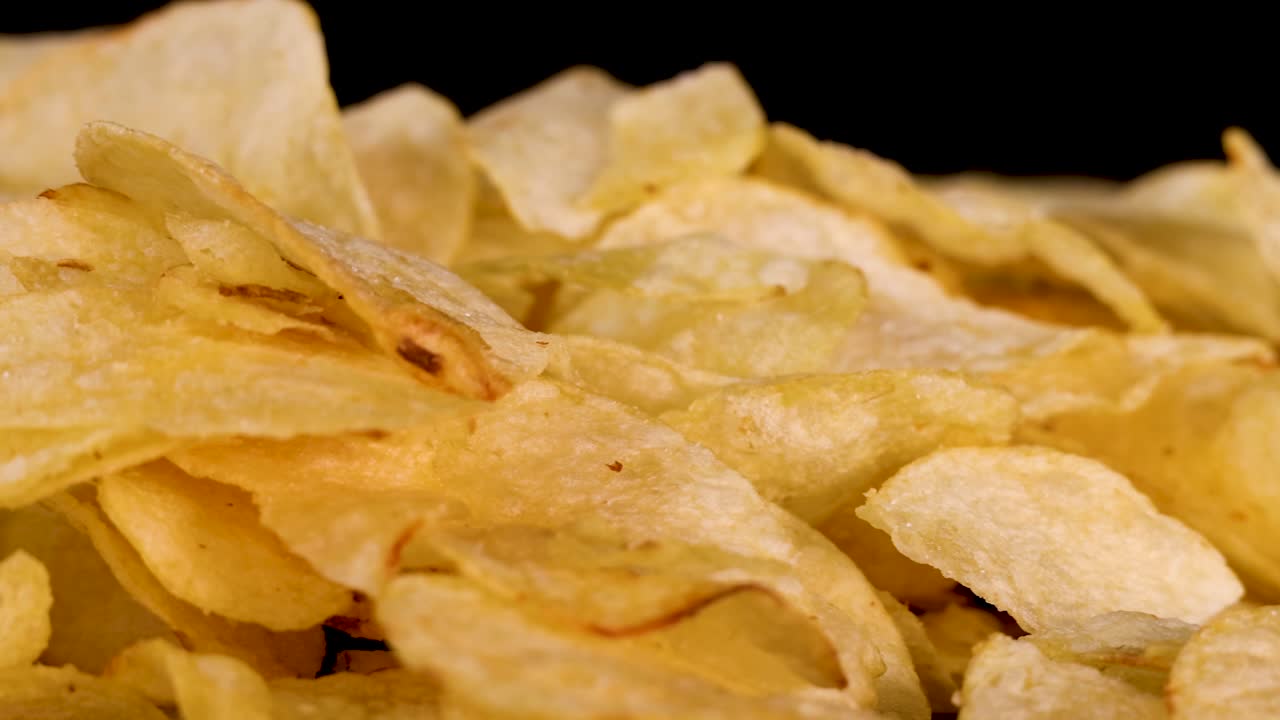 Golden potato chips rotate in close-up against black background, crisp texture highlighted by studio lighting