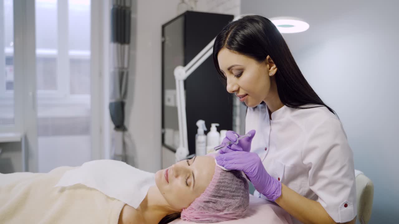 Young beautiful dark-haired woman gets rejuvenating facial injections. Work of the cosmetologist.