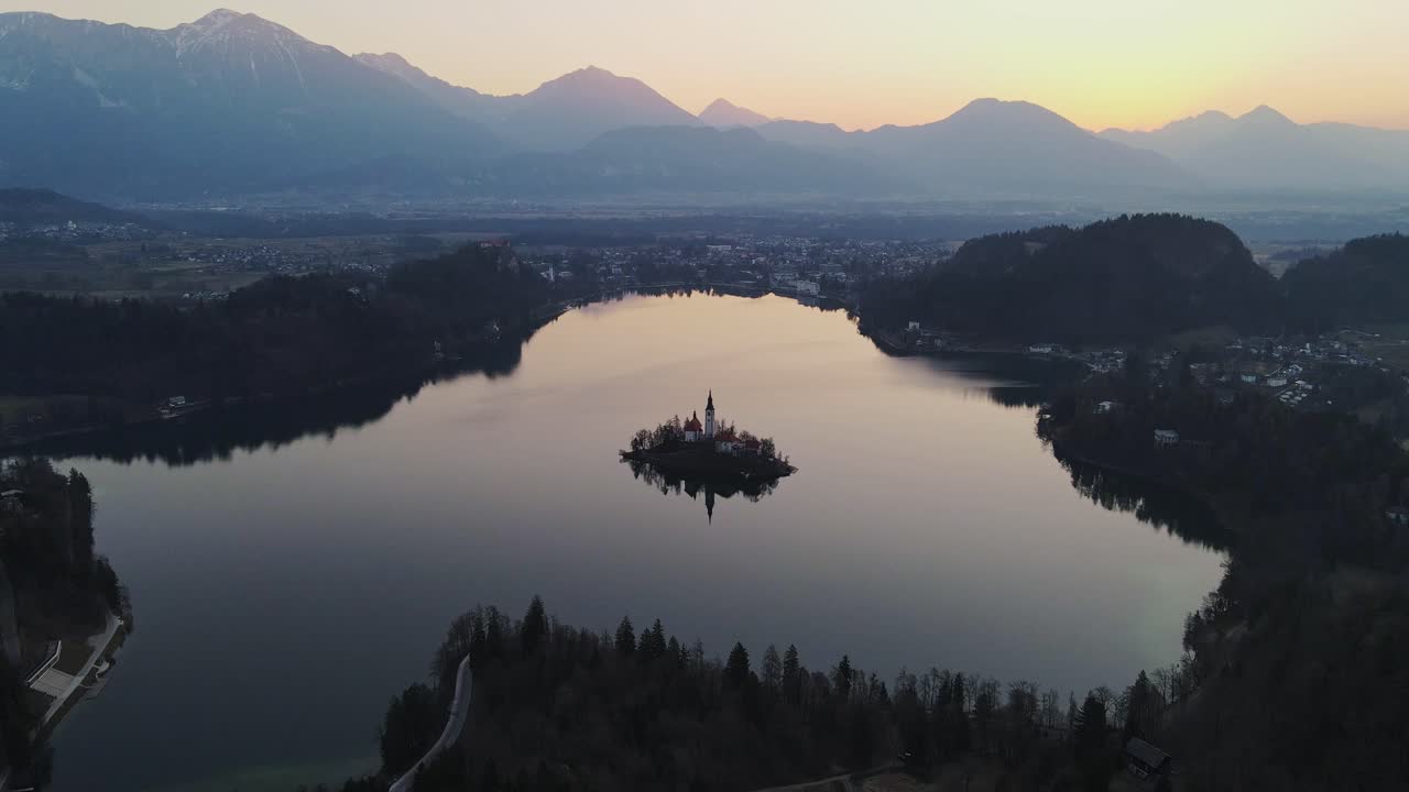 Soft golden glow of sunrise reflects on lake Bled iconic island church, spring