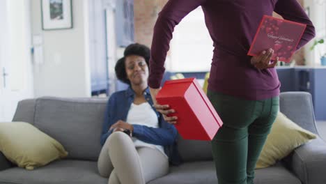 happy african american mother and daughter sitting on sofa, giving present