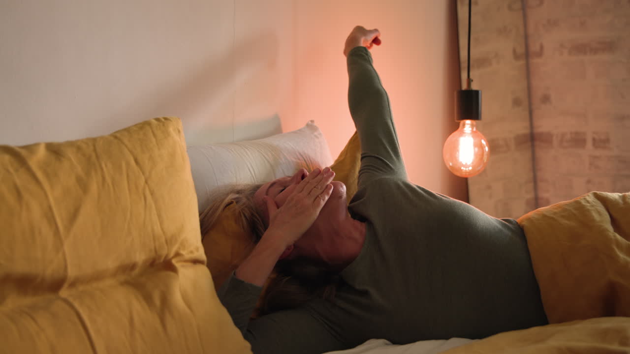 Relaxing in bed, senior woman smiling under warm light at home