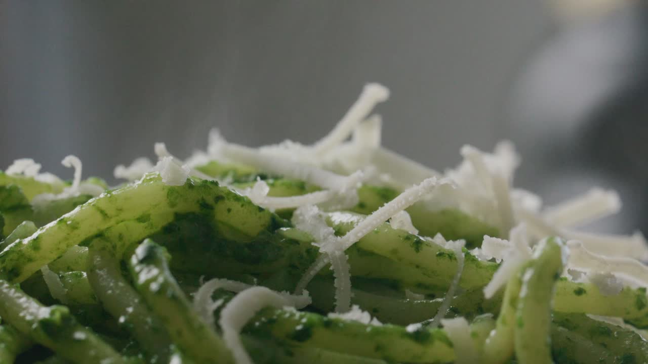 Shreds of Grated Cheese Falling and Melting on Hot Spaghetti with Spinach Sauce