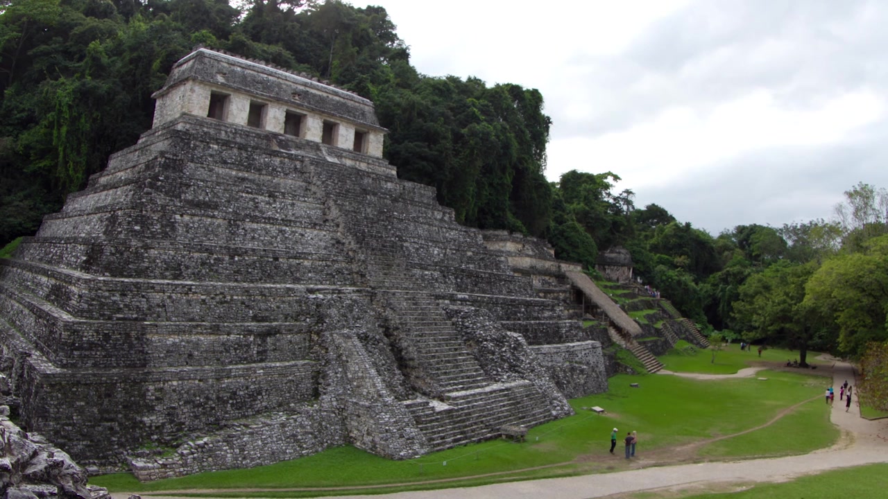 Storiche strutture in pietra mesoamericane e cortili erbosi si stagliano contro uno sfondo di fitta foresta