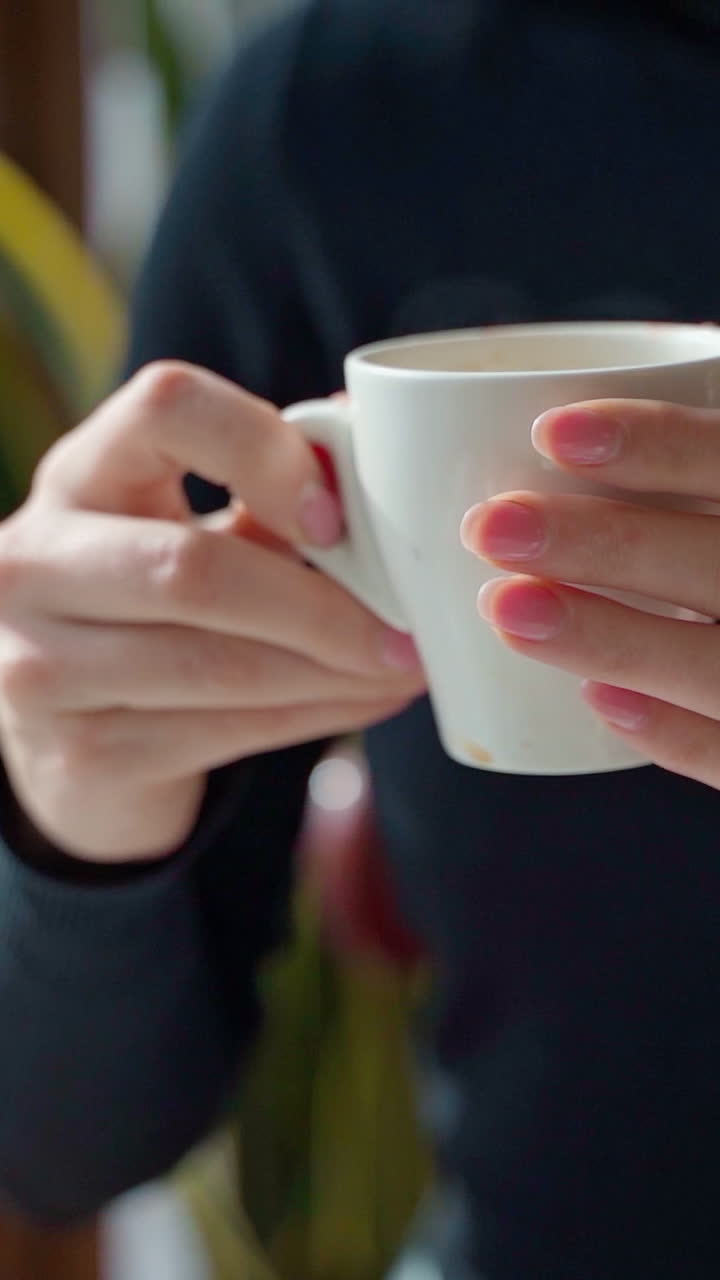 White cup with coffee in woman's hands. Beautiful young woman enjoying hot drink in a cafe. Slow motion. Vertical video
