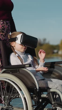 preschooler girl wearing vr headset plays game sitting in wheelchair. kid opens virtual door. mother stands near daughter on blurred background