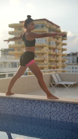 woman practicing yoga on a rooftop by a pool