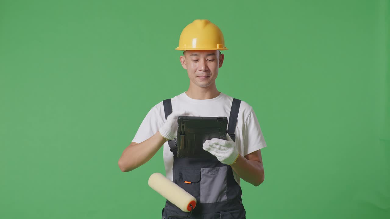 Asian Man Painter Wearing Safety Helmet Using A Tablet While Standing In The Green Screen Background Studio