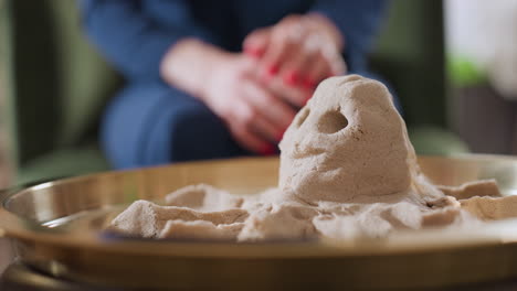 molded octopus figure crafted from soft sand rests in tray during therapy, with blurred background showing person seated in blue gown, adding emotional depth to calming sculpting session