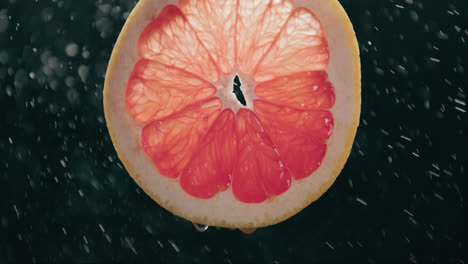 Frische-Grapefruitscheibe,-Die-Von-Wassertropfennebel-Mit-Flüssigkeitstropfen-In-Zeitlupe-Mit-Hintergrundbeleuchtung-Auf-Schwarzem-Hintergrund-Bespritzt-Wird