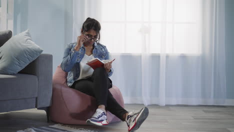 mujer india relajada lee un libro sentada en una silla de bolsa de frijol
