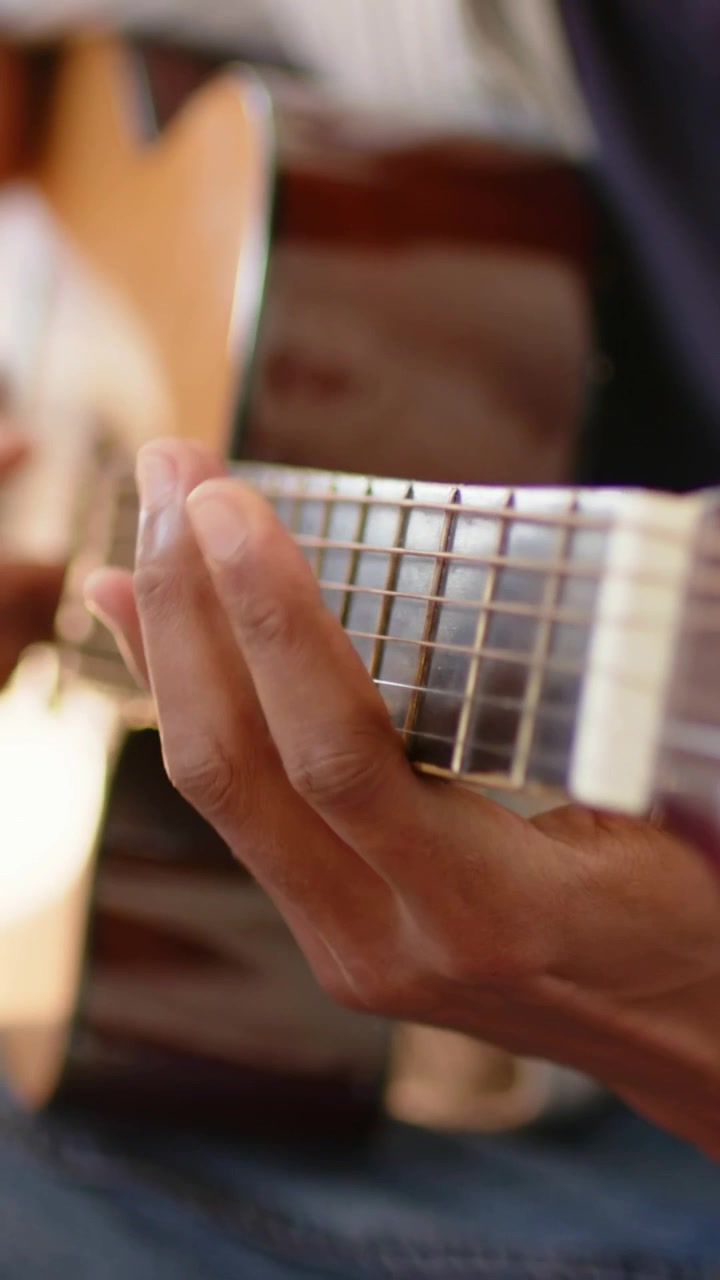 Vídeo vertical: Músico tocando, guiando a mão esquerda no braço de um violão acústico em casa, praticando.