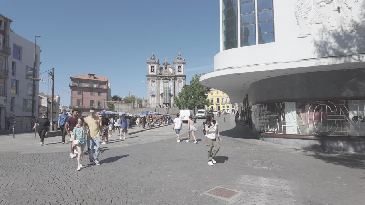 People walking through an outdoor market in a sunny square with wooden stalls in Porto