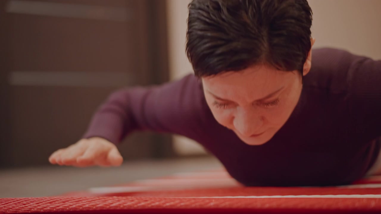 Female vocal student on red exercise mat practicing diaphragmatic breath control and vocal rest cozy studio environment, hands folded, eyes closed in concentration, quiet postrehearsal moment