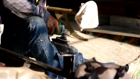 worker polishing metal part with grinding machine at workshop.