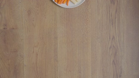 overhead view tracking down, of young girl sitting on cork floor with legs crossed, eating broccoli from a healthy plate of snacks, including tomatoes, carrots, grapes, cheese and crackers