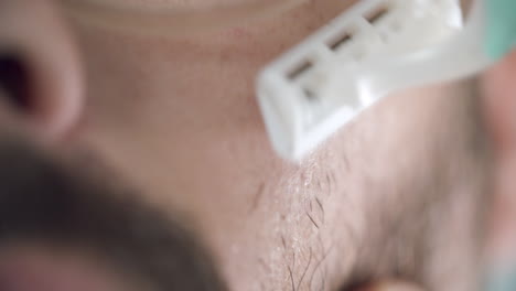 hombre afeitándose la mejilla izquierda con una navaja de una sola vez