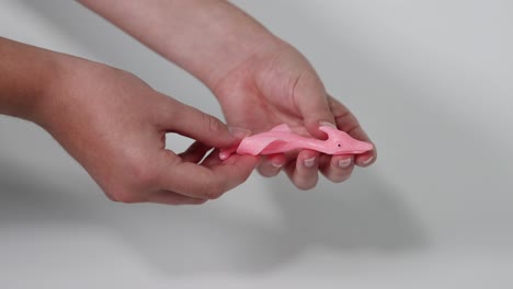 hands squishing a pink dinosaur toy together