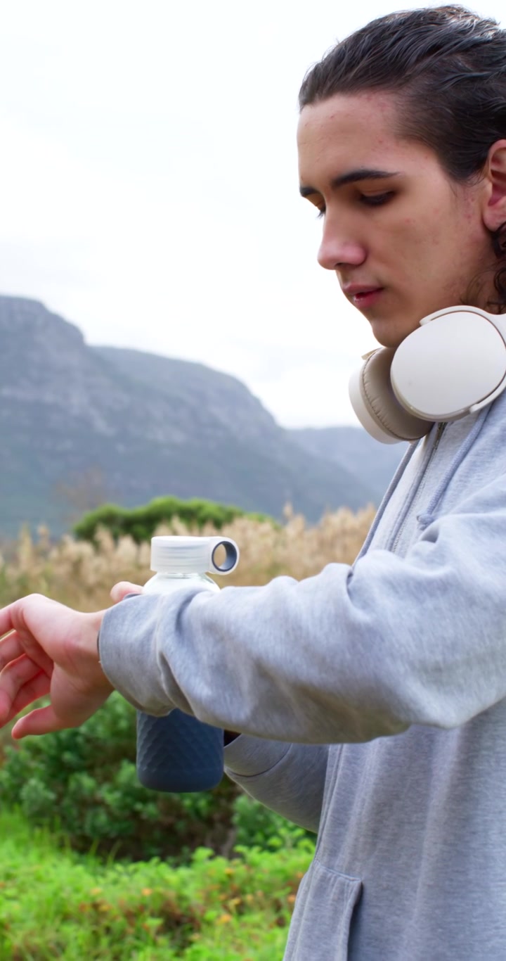 Vertical video: African American man unscrewing bottle cap, then checking smartwatch while hiking