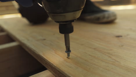 extreme close up of a man using a power drill to insert a screw into a sheet of plywood while building a skateboard ramp