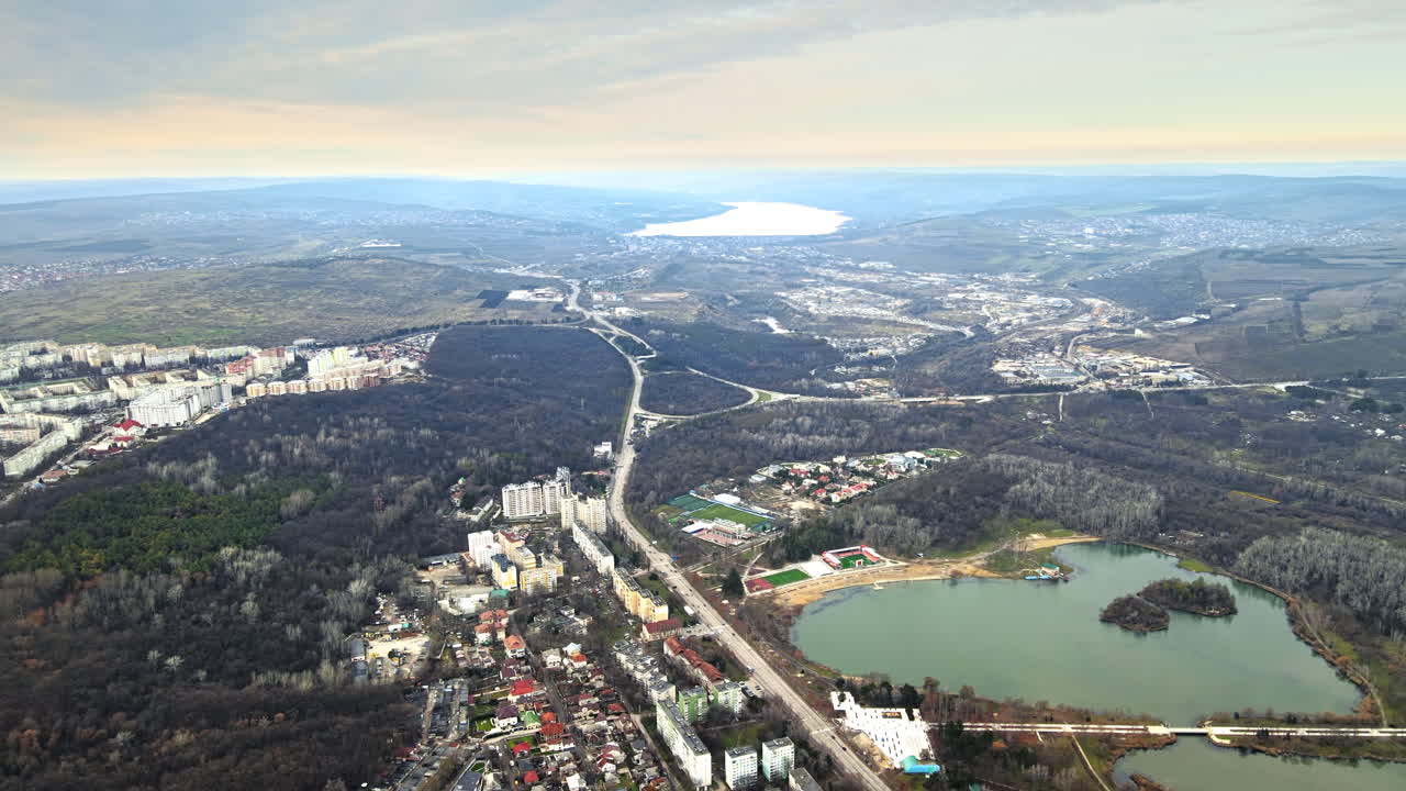Aerial drone view of Chisinau and suburban lands. Panorama view of buildings, road, hills covered with bare trees, two lakes, one in the distance. Good weather. Moldova