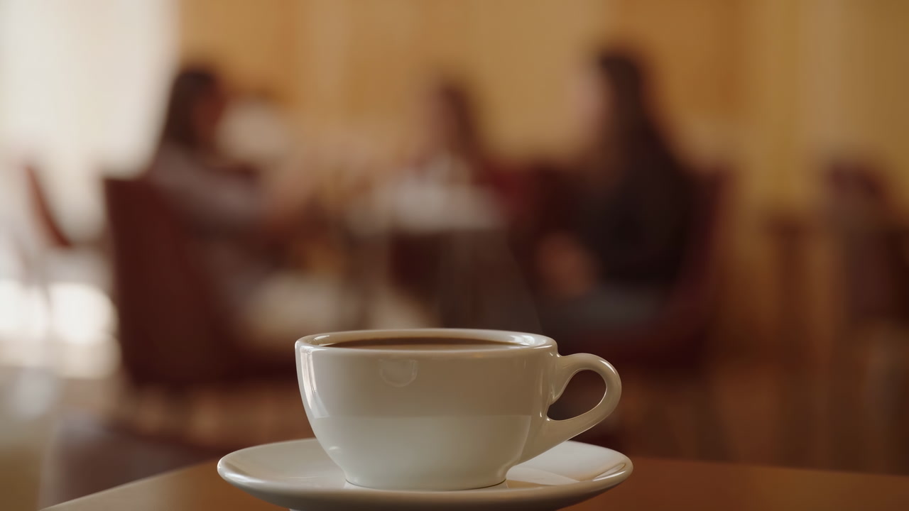 Closeup White Coffee Cup On Table With Blurred Colleagues Conversing In Warm Cafe, Steam Rising From Foam,
