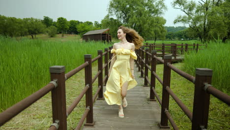 Beautiful-woman-in-sundress-running-towards-camera-on-wooden-boardwalk-in-park