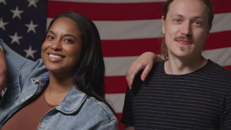 studio portrait shot of multi-cultural group of friends standing in front of american flag celebrating 4th july independence day