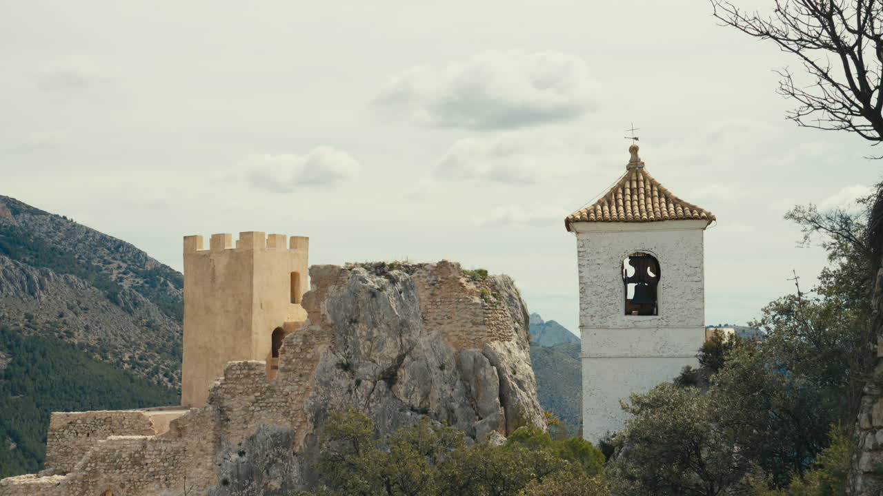 Vecchio campanile e antiche rovine di fortezza che si ergono su una scogliera rocciosa di montagna con uno scenario naturale suggestivo. Combinazione drammatica di storia, architettura e paesaggio aspro.