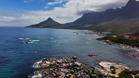south african stunning summer beach hommetjie bakoven beach view of table mountain lion's head drone aerial cinematic rugged boulder coastline white sand deep aqua blue ocean sea backward movement