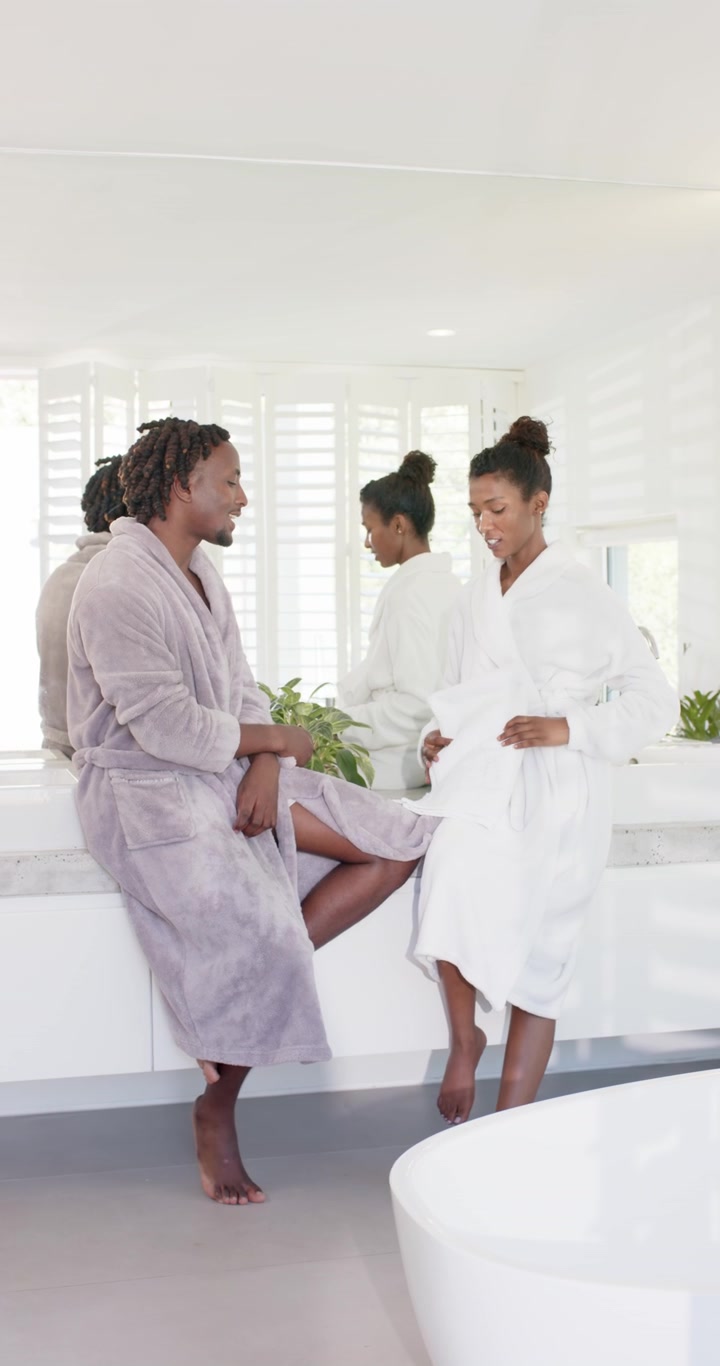 Vertical video: African American couple at bath vanity after bath, woman unfolding towel drying him