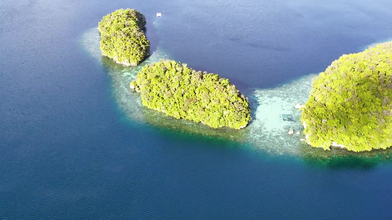 Uma tomada de drone em ângulo elevado move-se lentamente sobre ilhas de calcário verde exuberante cercadas por um oceano azul claro