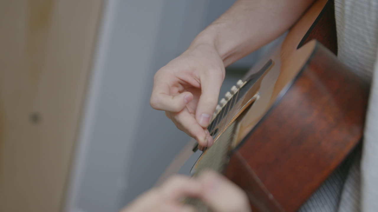 Slow motion footage looking down the neck of an acoustic guitar of a man picking at the strings
