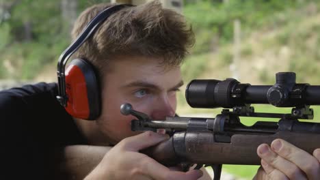 close-up van een man in oorbeschermers gericht op doel door te kijken naar de vergroting van de reikwijdte van een jachtgeweer op schietbaan